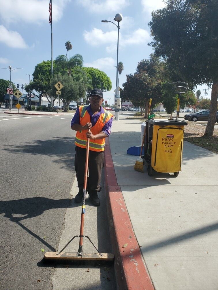 Crew member sweeping the sidewalk with a trash cart